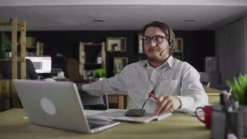 Young Manager in Headphones Is Working Looking in Smartphone in Office