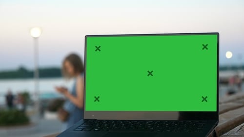 Laptop computer on street bench with green screen. Woman