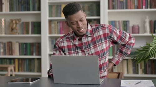 African Man having Back Pain while using Laptop in Office
