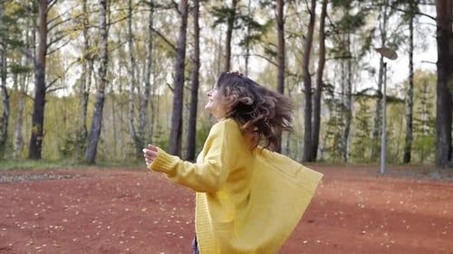 A Young Woman in a Yellow Sweater Walks in the Autumn Park. Brunette Woman Jumping and Dancing in