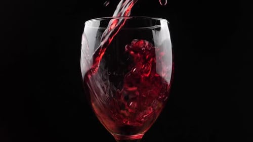 Wine. Red wine pouring in wine glass over dark background.