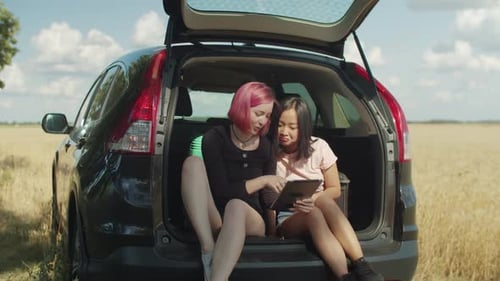 Two Young Adults Using Tablet in Car Trunk