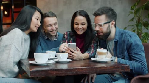 Cheerful Girls and Guys Using Smartphone Touching Screen Talking and Laughing in Cafe