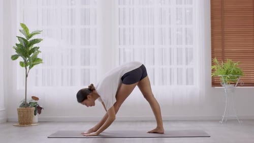 In the morning, an Asian woman is doing yoga, standing forward bend exercise