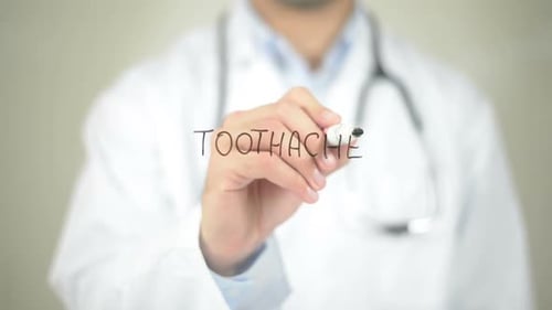 Doctor Writes the Word Toothache on Transparent Surface