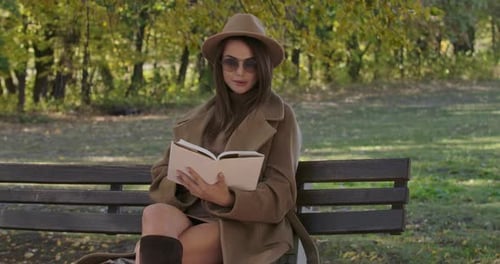 Woman Reading Book on Park Bench in Autumn