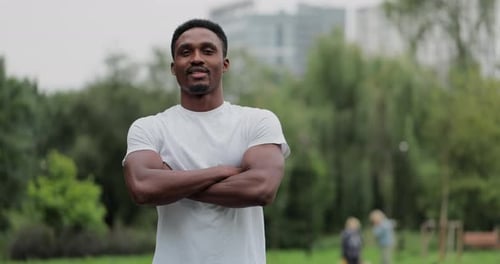 Joven afroamericano mira a la cámara sonriendo después de entrenar al aire libre con ejercicios corporales