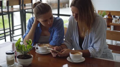 Women Having Date in Cafe. One Sharing Something Exciting on Her Mobile Phone