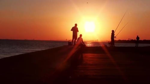 People Fishing on Pier at Colorful Ocean Sunset