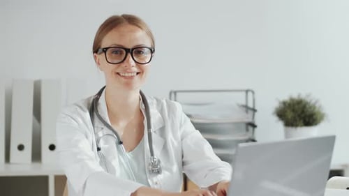 Female Doctor Smiling and Typing in Office
