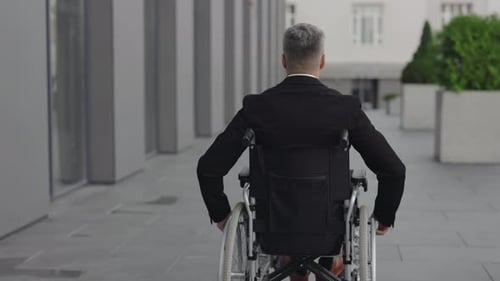 Backside View of Man in Suit Moving While Sitting in Wheel Chair at Street