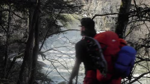 Male backpacker trekking next to white water river stream alone. Slow motion
