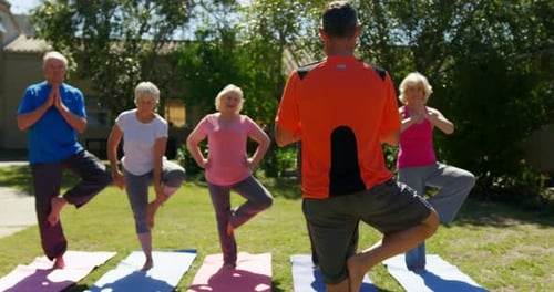Rear view of Caucasian male trainer training senior people in performing yoga at the garden of n 4k