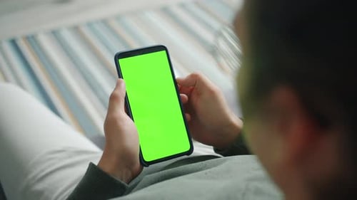 Man's Hand Holding Smartphone with Mock-up Green Chroma Key Screen in Apartment
