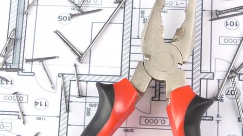 Gray and Red Pliers on Building Plan, Scheme Among Nails, Rotation, From Above