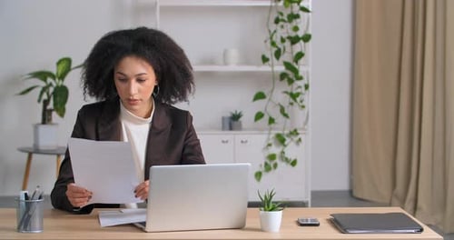 Young Adult Reviews Documents at Desk with Laptop