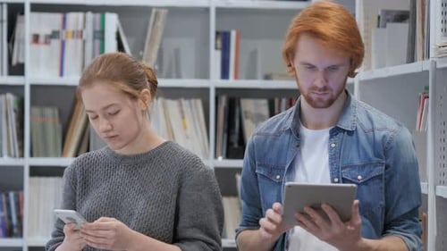 Redhead Man Using Tablet and Woman Using Smartphone in Office