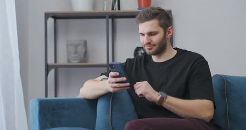 Young Man Using Smartphone on Couch at Home