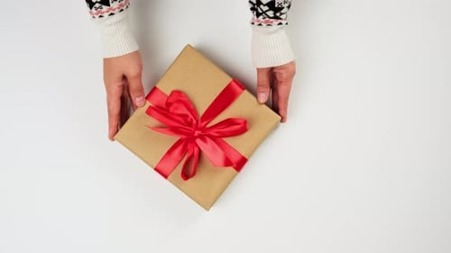 two female hands put on a white table a wrapped square box
