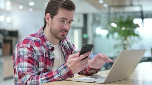 Young Adult Uses Laptop and Smartphone in Office