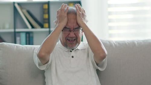 Senior Man Holds Head in Pain Indoors