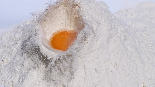 700017 Egg falling into flour against white background, Slow motion