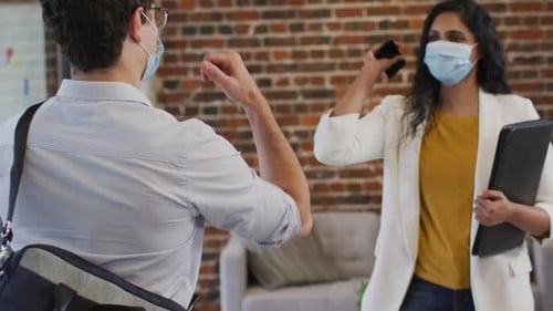 Man and woman wearing face masks greeting each other by touching their elbows at office