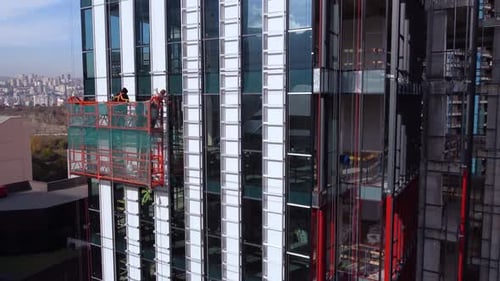 Arbeiter an der hängenden Wiege montieren die äußeren Elemente des Wolkenkratzers
