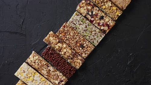 Various Healthy Granola Bars Placed in a Row on Black Stone Table
