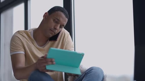 Busy African American Man Talking on the Phone Surfing Internet on Tablet in Home Office