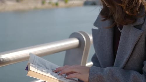 Woman Reading a Book Outdoors by the Water