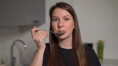 Woman Tastes Food from a Spoon in Kitchen