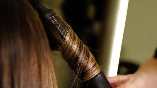 Friseur macht Locken aus Kundenhaaren mit Lockenstab