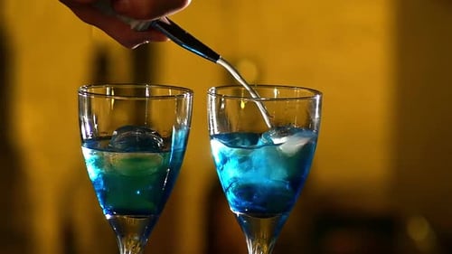 Barman Making Cocktails at the Night Club, Using Two Glasses with Ice Adding Cloudy White Liquid
