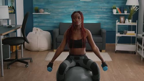 Woman Lifts Weights on Exercise Ball in Home