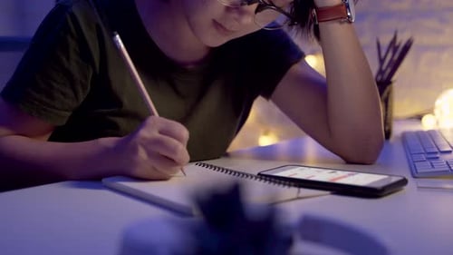 Las manos femeninas escriben en un cuaderno y usan un teléfono inteligente por la noche