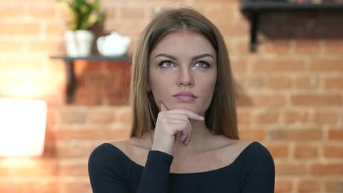 Thoughtful Young Woman Posing Indoors in Front of Brick Wall