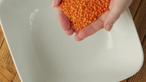 Orange Lentils Pouring Into White Bowl