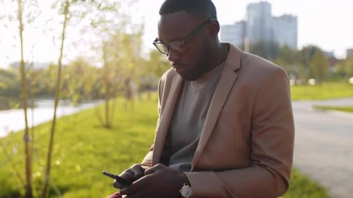 Afroamerikanischer Mann benutzt Smartphone im Freien am Flussufer