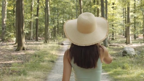 Woman Walks Along Sunny Forest Trail in Sunhat