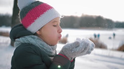 Happy Girl Blowing Snowflakes in Winter Landscape