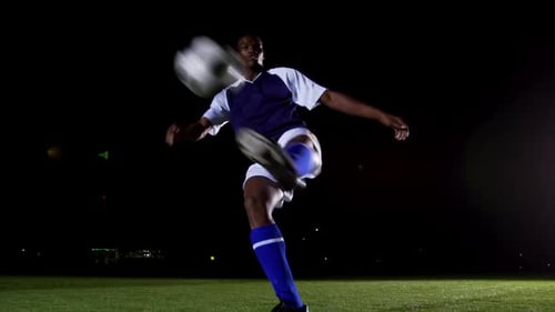 Man Kicks Soccer Ball on Field at Night