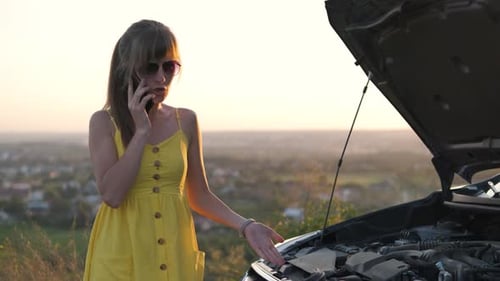 Stranded Female Driver Talking on Cell Phone Standing Near Her Vehicle with Open Hood Having Engine