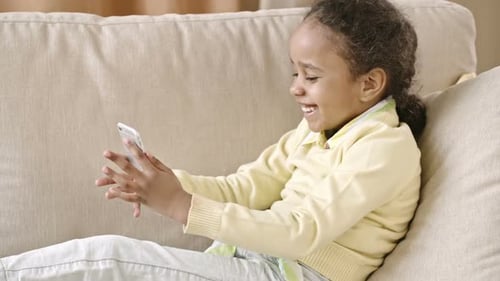 Happy Girl Enjoys Smartphone on Couch at Home