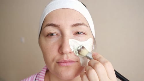 Junge Frau trägt Kosmetikmaske mit einem Pinsel auf das Gesicht auf