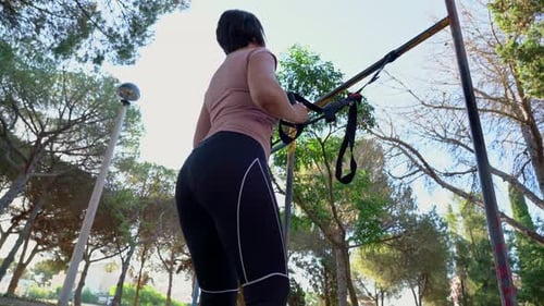 Woman Exercising and Squatting Outside at a Park with Suspension Straps