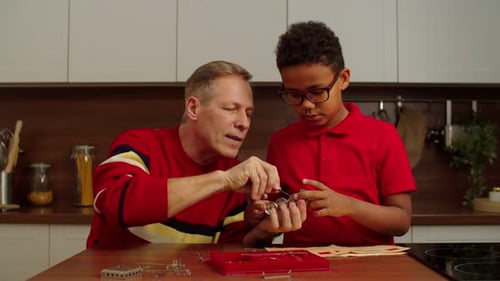 Grandpa and School Age Black Grandson Assembling Toy From Metallic Constructor