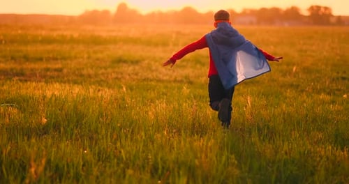 Boy in Superhero Costume and Mask Running Across the Field at Sunset Dreaming and Fantasizing