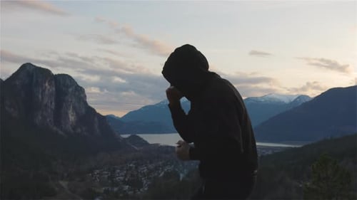 Hooded Person Boxing in a Mountainous Landscape