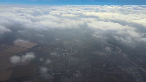 Aerial View From High Altitude of Distant City Covered with Puffy Cumulus Clouds Flying By Before